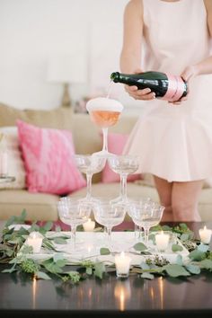 a woman pouring champagne into wine glasses on top of a table with candles and greenery