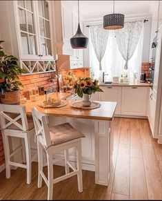 a kitchen with white cabinets and wooden flooring next to a table filled with flowers