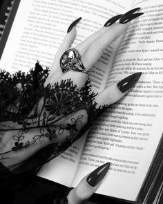 a woman's hand with black nail polish holding an open book in front of her face