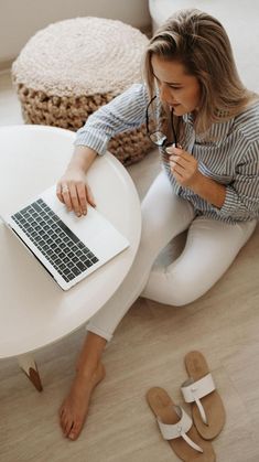 a woman is sitting on the floor with her laptop and sandal wedges in front of her