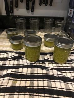 six jars filled with pickles sitting on top of a checkered table cloth next to knives