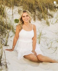 a woman is sitting in the sand with her legs crossed and wearing a white dress