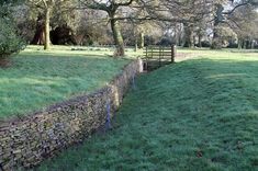 a stone wall in the middle of a field with trees and grass on both sides