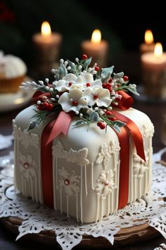 a white cake decorated with red ribbon and flowers on a doily next to lit candles