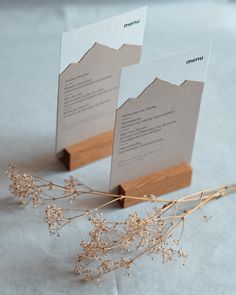 two place cards are placed on top of each other, with dried flowers in the foreground