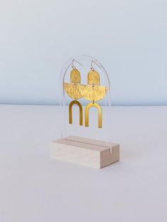 a pair of gold earrings sitting on top of a wooden stand