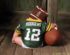 a baby sitting on the floor with a football in his hands and wearing a green jersey