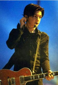 a young man holding a guitar and talking on a cell phone while standing in front of a microphone