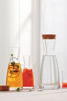 three glass vases with different types of liquid in them on a white table next to a window