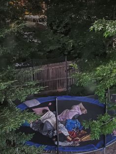 a man laying on top of a blue trampoline in the middle of trees