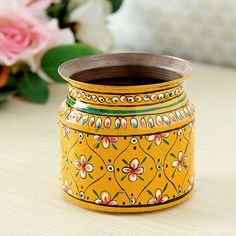 a yellow vase sitting on top of a wooden table next to pink and white flowers