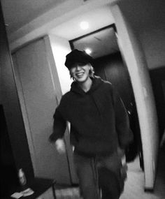 black and white photograph of a man walking through a hallway with a hat on his head