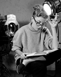 a woman sitting in a chair reading a book while holding a light up to her face