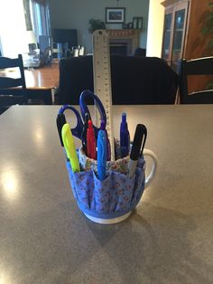 a cup filled with pens and scissors on top of a table next to a ruler