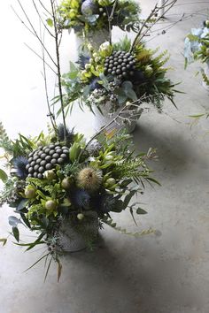 three vases filled with different types of flowers and greenery sitting on a table