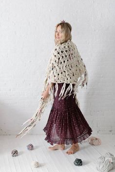 a woman wearing a crochet shawl and standing in front of a white wall