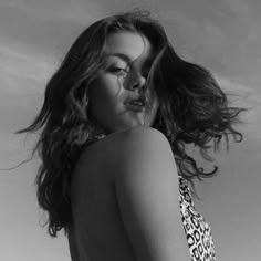 a woman in a leopard print swimsuit standing on the beach with her hair blowing in the wind