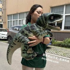 a woman holding a stuffed alligator in front of a building with cars parked on the street behind her