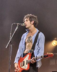 a shirtless man holding an electric guitar in front of a microphone