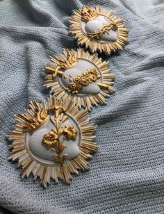 three gold and white brooches sitting on top of a blue blanket