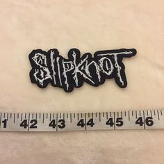 a black and white patch with the word slipknot on it next to a measuring tape