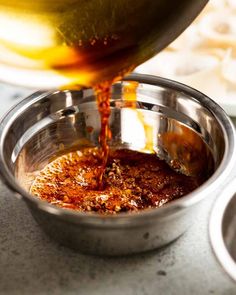 a person pouring sauce into a metal bowl