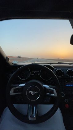 the inside view of a car driving on a highway at sunset or dawn with an ocean in the background