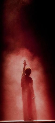 a man standing in front of a red light with his hands up to the sky