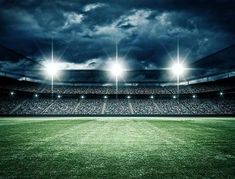 an empty football stadium with the lights on and dark clouds in the sky over it