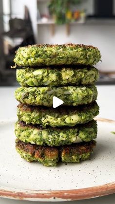 a stack of broccoli patties sitting on top of a white plate next to a potted plant