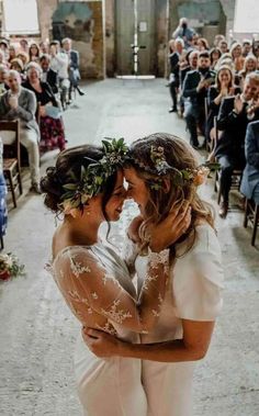 two brides hugging each other in front of an audience at a wedding ceremony with flowers on their heads