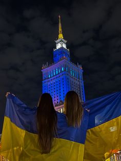 two women standing in front of a tall building with a blue and yellow flag on it