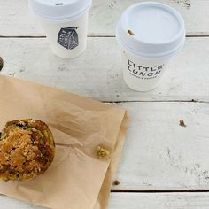 a muffin sitting on top of a piece of paper next to two cups of coffee