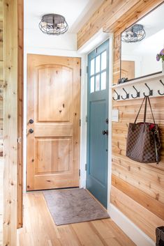 a blue door is in front of a wood paneled entryway with a handbag hanging on the wall