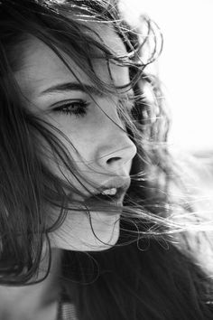 black and white photograph of a woman with her hair blowing in the wind, looking at the camera