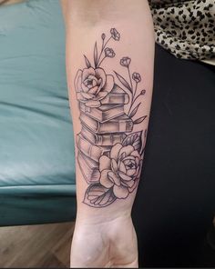 a person with a tattoo on their arm holding a stack of books and flowers in front of them