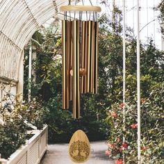 a wooden wind chime hanging from the ceiling in a garden filled with trees and plants