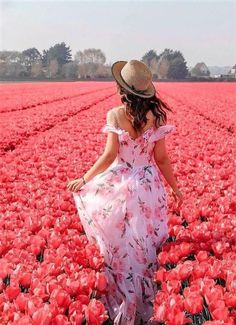 a woman in a dress and hat walking through a field full of red tulips