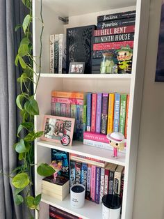 a bookshelf filled with lots of books next to a potted green plant