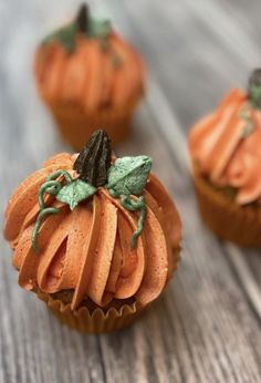 three cupcakes decorated with orange icing and green leaf decorations on wooden table