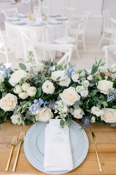 the table is set with white and blue flowers, greenery, and silverware