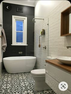 a white bath tub sitting next to a toilet under a bathroom window on top of a tiled floor