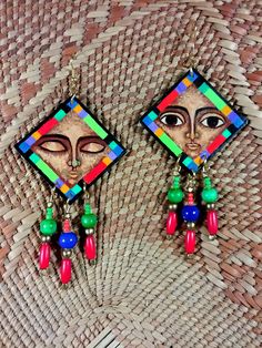 "These multi-colored diamond shaped earrings show influences of archaic  native designs. The vibrant color scheme and geometric designs are complemented with neutral facial features.  One open-eyed and the other closed eyed.  Accent beads are blue, green, red and brass. Dimensions are 2 1/8\" by 2 1/8\".  Signed by the artist." Bohemian Multicolor Rectangular Jewelry, Unique Multicolor Earrings For Festivals, Bohemian Rectangular Earrings, Bohemian Multicolor Rectangular Earrings, Artistic Multicolor Earrings With Colorful Design, Bohemian Multicolor Artistic Design Jewelry, Bohemian Multicolor Artistic Jewelry, Artsy Multicolor Rectangular Earrings, Unique Multicolor Geometric Jewelry