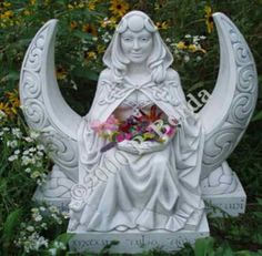 a white statue sitting on top of a lush green field next to flowers and plants