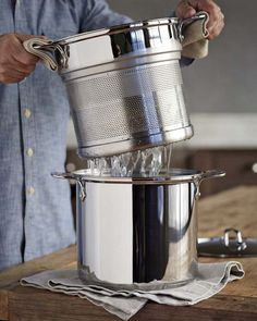 a man pouring water into a large pot on top of a wooden table next to a knife