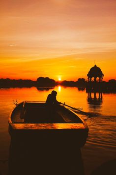 a person in a rowboat on the water at sunset with an gazebo in the background