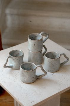 four white ceramic cups sitting on top of a table next to a vase and chair