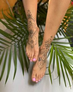 a woman's feet with tattoos on them and palm leaves in the foreground