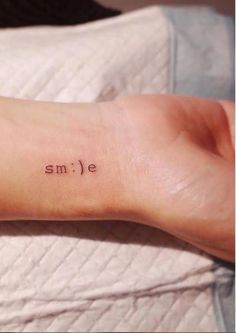 a small smile tattoo on the left inner arm and wrist is shown in black ink