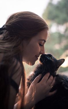 a woman is holding a black cat and kissing it's face with her eyes closed